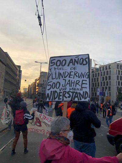 Eine Demonstrantin hält ein Schild hoch mit der Aufschrift "500 Años Maschine de Plünderung 500 Años Maschine de Widerstand"