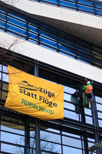 An der Fassade des Willy-Brandt-Hauses hängt ein Robin-Wood-Aktivist in Kletterausrüstung mit einem Transparent auf dem "Züge statt Flüge" steht.