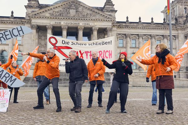Vor dem Reichstagsgebäude singen mehrere Menschen, dahinter Attacies mit Fahnen zu sehen.